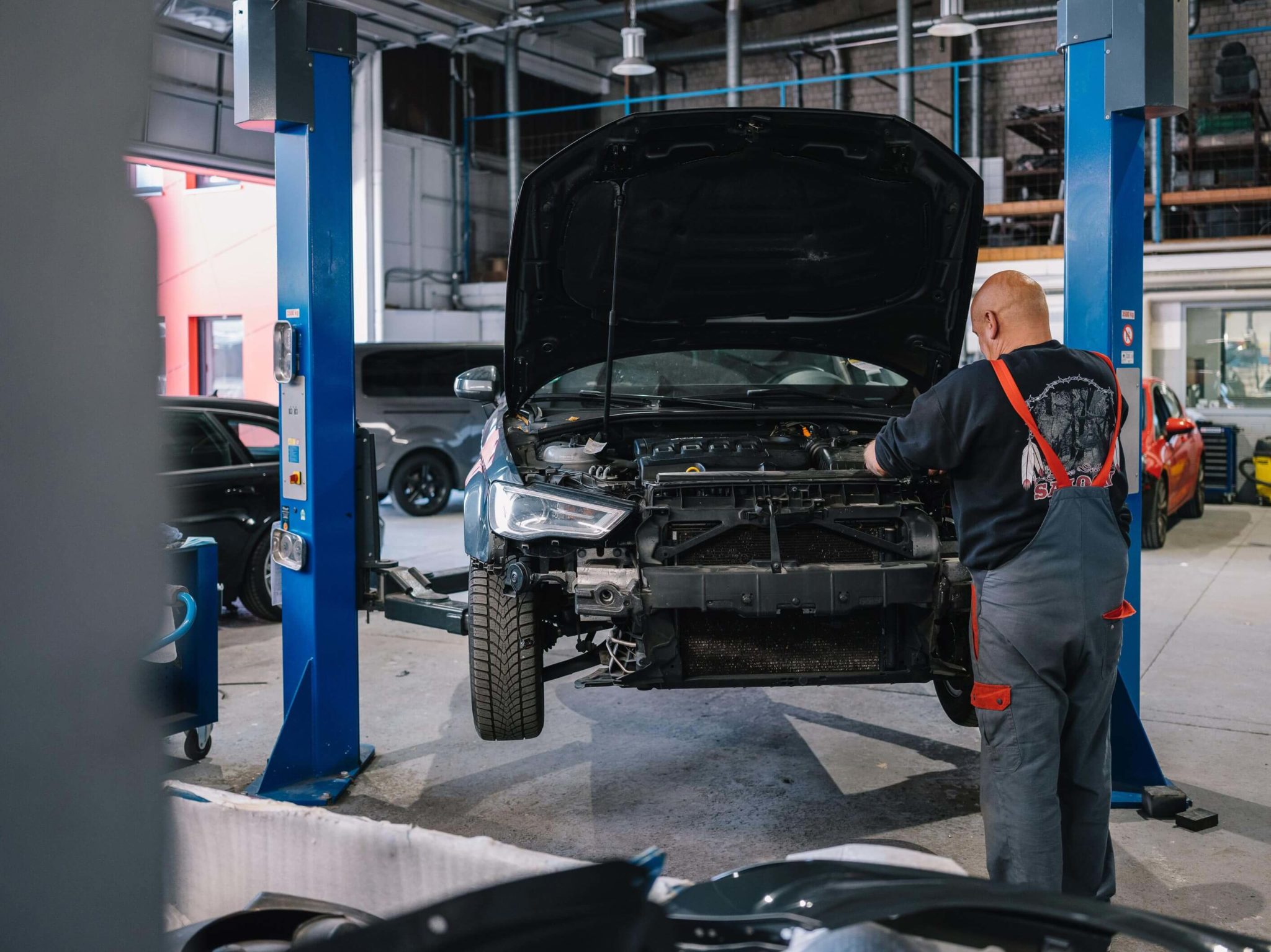 Werkstattmitarbeiter inspiziert ein hochgebocktes Auto in der Motorhaube